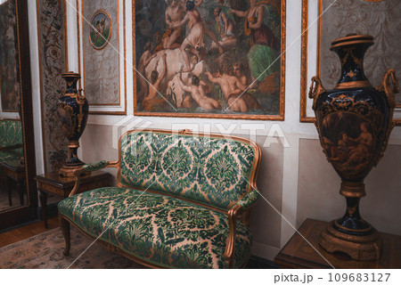 Experience the opulence and grandeur of a Venetian-inspired room with ornate couches, vases, and paintings. The green and gold color scheme creates a luxurious and elegant ambiance. 109683127