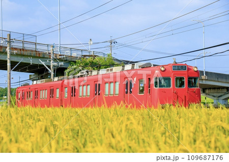 収穫期の田園地帯を走る名鉄三河線電車 109687176