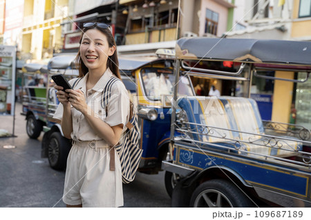 Happy young travel Asian woman using a mobile phone in a street market at dusk in Bangkok, Thailand, Travel vacation city concept 109687189