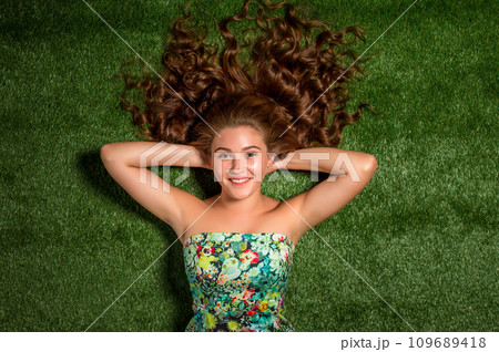 Portrait of pretty smiling young woman, laying on the grass 109689418