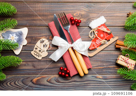 Top view of christmas decorations on wooden background. Close up of fork and knife on napkin tied up with ribbon. New year pattern concept 109691106