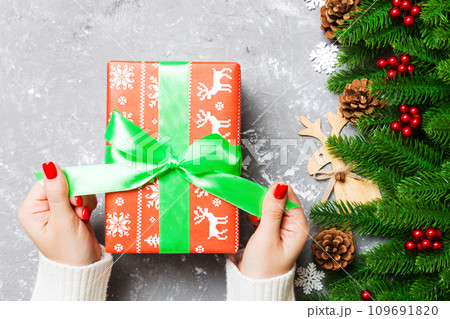 Top view of female hand tie up New Year present on festive wooden background. Fir tree and holiday decorations. Christmas time concept 109691820
