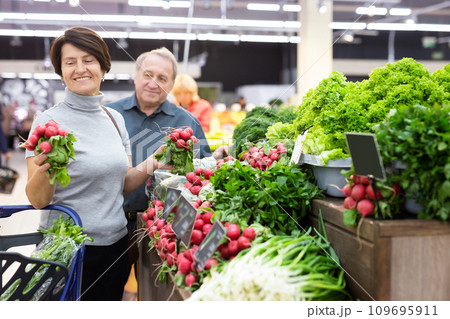 Smiling happy couple is choosing bell peppers and other vegetables in supermarket 109695911