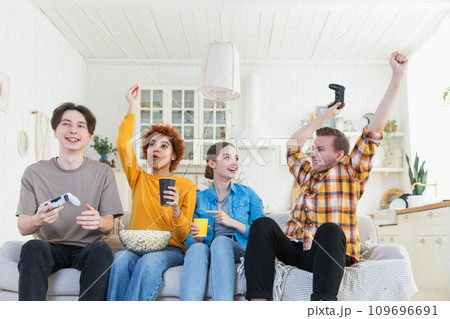Home party. Cheerful group of friends playing video games at home. Happy diverse group buddies having fun together indoor. Friendship leisure entertainment concept. Young best friends enjoying weekend 109696691