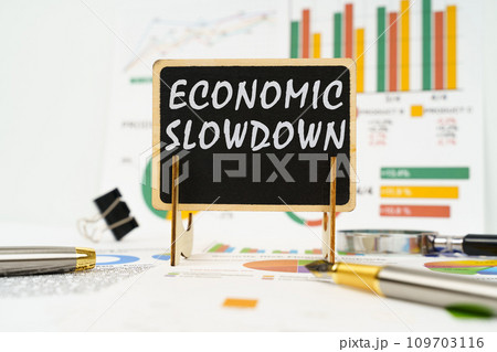 Against the background of business graphs, a board with the inscription - economic slowdown 109703116