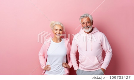 Elderly couple aktive seniors in pink hoodie stands smiling against soft pink background. They both exemplify active and joyful healthy aging. Senior Fitness. Elderly couple aktive seniors in pink hoodie stands smiling against soft pink background. They both exemplify active and joyful healthy aging. Senior Fitness. 109703427