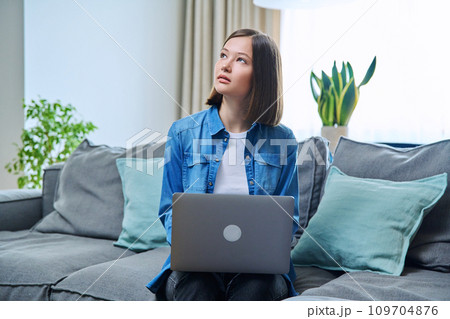 Young woman sitting on living room sofa at home with laptop 109704876