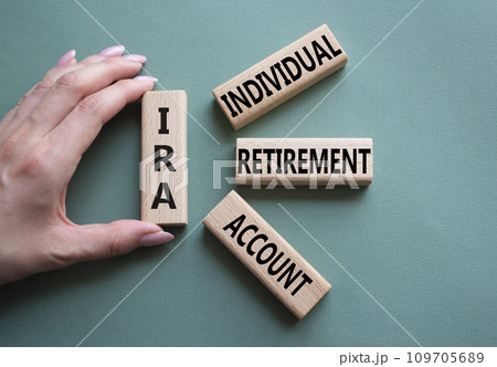 IRA - Individual Retirement Account symbol. Concept word IRA on wooden blocks. Businessman hand. Beautiful grey green background. Business and IRA concept. Copy space. 109705689