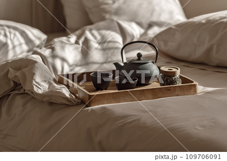 Black cast iron tea pot with herbal tea set up on wood tray on the bed. Traditional Asian Tea Set - iron teapot and ceramic teacups with green tea and tea leaves. Black cast iron tea pot with herbal tea set up on wood tray on the bed. Traditional Asian Tea Set - iron teapot and ceramic teacups with green tea and tea leaves. 109706091