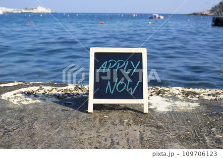 Apply now symbol. Concept word Apply now on black chalk blackboard. Beautiful sea background. Business and Apply now concept. Copy space Apply now symbol. Concept word Apply now on black chalk blackboard. Beautiful sea background. Business and Apply now concept. Copy space 109706123