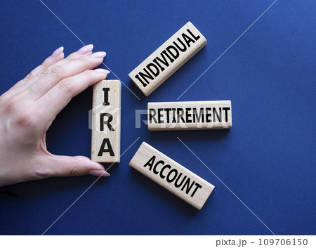 IRA - Individual Retirement Account symbol. Concept word IRA on wooden blocks. Businessman hand. Beautiful deep blue background. Business and IRA concept. Copy space. 109706150