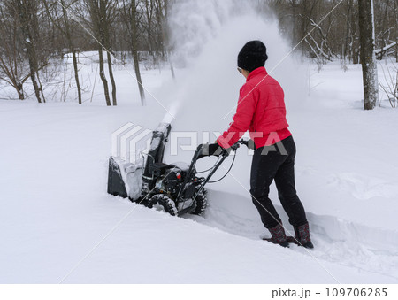 A young woman clears snow with snow removal equipment after a heavy snowfall 109706285