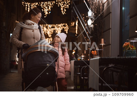Happy mother and daughter strolling the street together, enjoying the walk in the night time during Christmas funfair 109709960