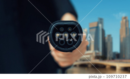 EV charger pointing in front of camera with city background. Peruse EV charger pointing in front of camera with city background. Peruse 109710237