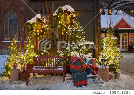 Christmas decorations - bench, Christmas trees, gift boxes, garlands and lights. Festive Christmas decoration at the Dome Square in old Riga city. Riga, Latvia. Snowy New Year's photo location. 109711889
