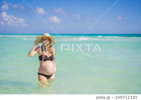 Radiant and expecting, a pregnant woman stands on a pristine snow-white tropical beach, celebrating the miracle of life against a backdrop of natural beauty Radiant and expecting, a pregnant woman stands on a pristine snow-white tropical beach, celebrating the miracle of life against a backdrop of natural beauty 109712385