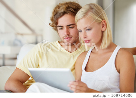 Reading, tablet and young couple on sofa browsing on social media or internet at apartment. Relax, digital technology and man and woman from Australia scroll on website in living room at home. 109714606