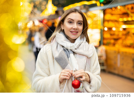 Portrait of girl with gift bag choosing Christmas tree balls Portrait of girl with gift bag choosing Christmas tree balls 109715936