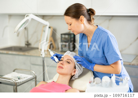Adult woman cosmetologist doing microcurrent procedure to young woman Adult woman cosmetologist doing microcurrent procedure to young woman 109716117