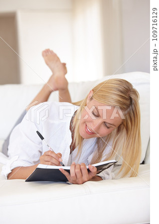 Writing, notebook and relax with woman on sofa for goals, diary and schedule. Calendar, planning and list with female person and journal in living room of home for self care, reflection and idea 109716129