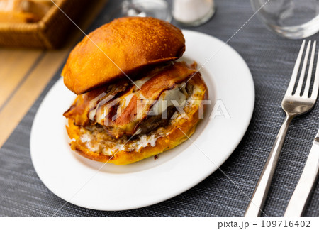 Burger in wheat bun with veal patty, cheese slice and fried bacon Burger in wheat bun with veal patty, cheese slice and fried bacon 109716402