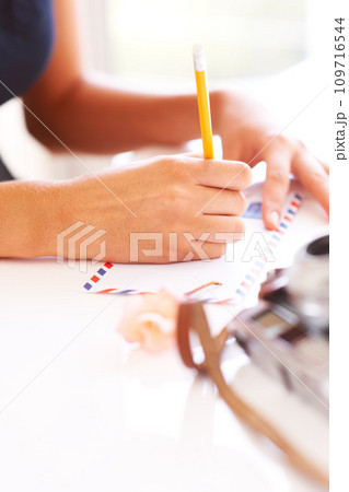 Hands, pencil and writing on letter on table, thought and communication for envelope in apartment. Young person, paper message and mail with idea, thinking and courier to post vintage note in home Hands, pencil and writing on letter on table, thought and communication for envelope in apartment. Young person, paper message and mail with idea, thinking and courier to post vintage note in home 109716544
