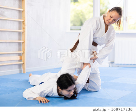 Sportive woman holds her opponent by force while sitting on mats during judo classes 109717236
