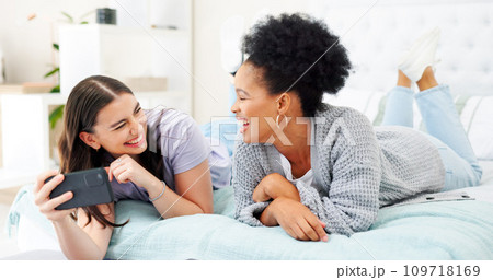 Phone, social media and woman friends laughing on bed together while looking at an internet meme. Smile, diversity and comedy with funny young people joking in the bedroom of a home in the morning 109718169
