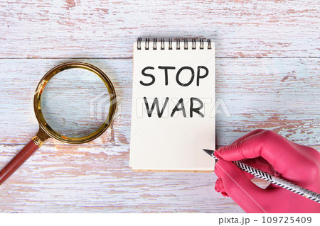 STOP WAR writing on a notebook lying on old boards next to a magnifying glass and a hand in a red medical glove with a pencil 109725409