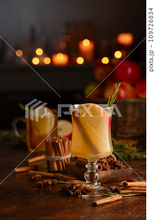 Mulled cider with apples, cinnamon, rosemary, and anise on a background of burning candles. Mulled cider with apples, cinnamon, rosemary, and anise on a background of burning candles. 109726834
