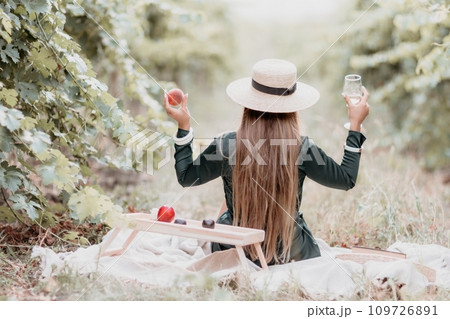 Woman picnic vineyard. Happy woman with a glass of wine at a picnic in the vineyard, wine tasting at sunset and open nature in the summer. Romantic dinner, fruit and wine. 109726891