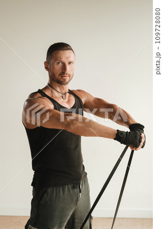 A man in black sportswear is engaged in strength fitness using a rubber loop indoors A man in black sportswear is engaged in strength fitness using a rubber loop indoors 109728080
