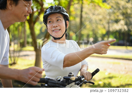 Happy senior couple walking with bicycle talking at summer city park. Retirement lifestyle concept. Happy senior couple walking with bicycle talking at summer city park. Retirement lifestyle concept. 109732382