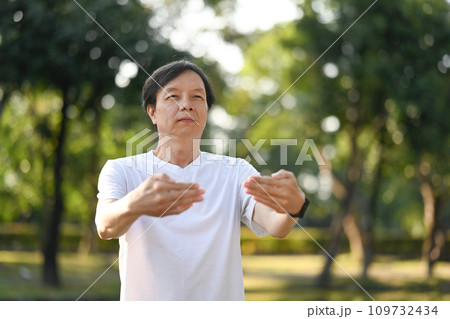 Calm middle age Asian man practicing Qigong in the park at sunrise. Healthy lifestyle concept. Calm middle age Asian man practicing Qigong in the park at sunrise. Healthy lifestyle concept. 109732434