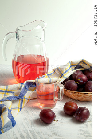 Plum Compote in jug with purple plums on white wooden background. . Plum Compote in jug with purple plums on white wooden background. . 109735116