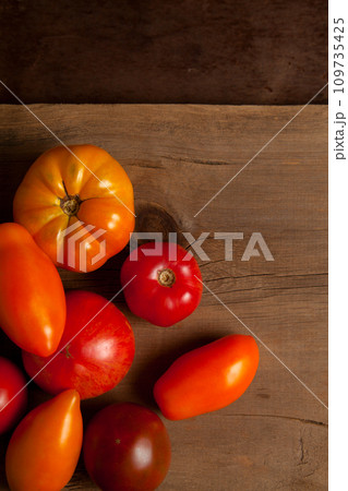 Assort of different shape and color tomatoes on wooden background with red kitchen towel.. Assort of different shape and color tomatoes on wooden background with red kitchen towel.. 109735425