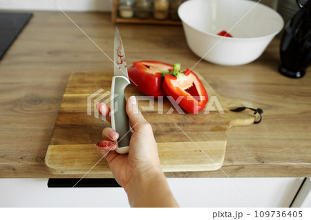 Woman cut her little finger with a knife while cooking vegetable salad on the kitchen. Female hand with blood holds knife with a sharp blade resulted in a cut and wounded finger cooking accident. Woman cut her little finger with a knife while cooking vegetable salad on the kitchen. Female hand with blood holds knife with a sharp blade resulted in a cut and wounded finger cooking accident. 109736405