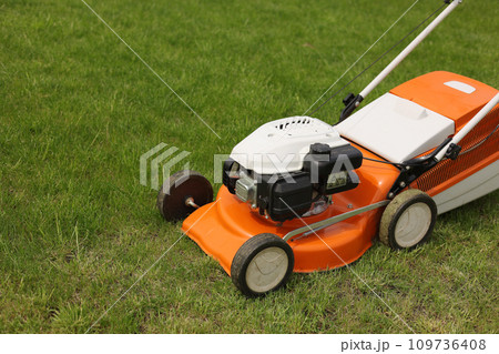 Close up orange-grey electric lawn mower on bright lush green lawn. Gardening work tools. Rotary lawn mower machine cut grass. Professional lawn care service. Place for text Close up orange-grey electric lawn mower on bright lush green lawn. Gardening work tools. Rotary lawn mower machine cut grass. Professional lawn care service. Place for text 109736408
