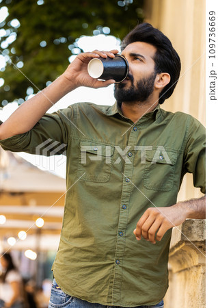 Adult indian man enjoying drinking morning coffee hot drink, relaxing, taking a break in city street 109736669