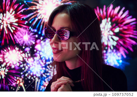 Beautiful young woman in sunglasses looking on fireworks. Lights reflection on eyewear. Holiday celebration 109737052