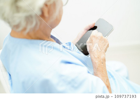 Asian senior woman wearing eyeglasses or vision glasses using a smartphone at home care service. 109737193