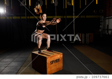 Athletic woman in sportswear jumping on crossfit box in fitness gym 109737661