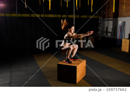 Athletic woman in sportswear jumping on crossfit box in fitness gym 109737662