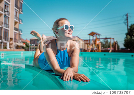 Bikini-clad woman enjoys poolside relaxation. Poolside ambiance. Capturing woman's relaxed time near pool. Bikini-clad woman enjoys poolside relaxation. Poolside ambiance. Capturing woman's relaxed time near pool. 109738707