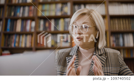 Serious woman talking over earbuds, conducting an online lesson in the library, busy teacher 109740502