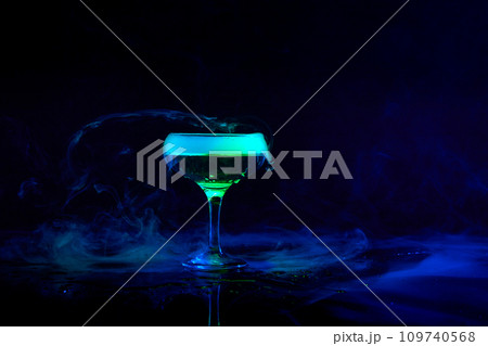 Glass with alcohol cocktail, martini with smoke foam against dark background with neon light. Bartender 109740568