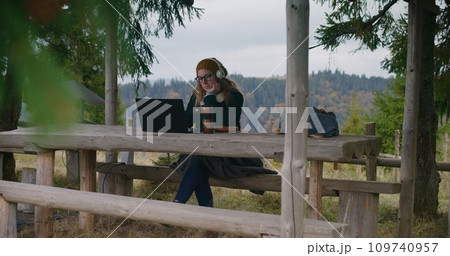 Adult woman in headphones listens music in wooden gazebo Adult woman in headphones listens music in wooden gazebo 109740957