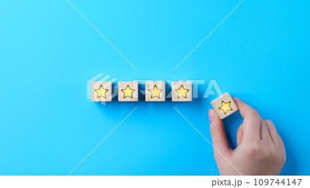 Customer review satisfaction feedback survey concept. Hand put wooden cube block with yellow star icon on blue background. Client questionnaire, Service rating user, Business evaluation, 5, Five star, 109744147