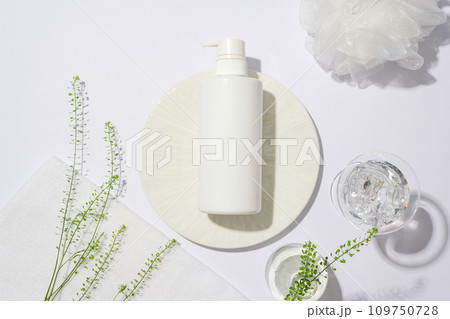 Close-up of a bottle of shower gel placed on a round white podium, surrounded by decorative flowers and props on a pure white background. Space for advertising. Close-up of a bottle of shower gel placed on a round white podium, surrounded by decorative flowers and props on a pure white background. Space for advertising. 109750728