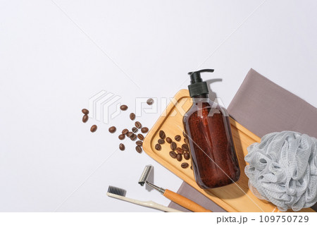 A brown shampoo bottle is displayed on a wooden tray with coffee beans on a white background. Empty space for text design. View from above, copy space. A brown shampoo bottle is displayed on a wooden tray with coffee beans on a white background. Empty space for text design. View from above, copy space. 109750729